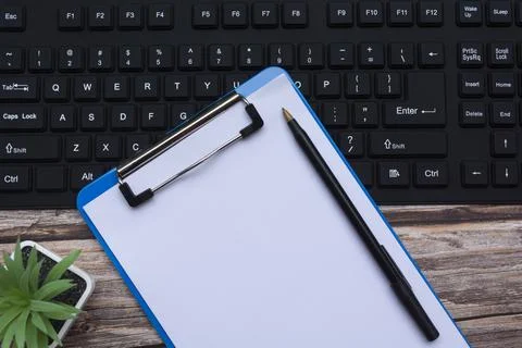 Home office workspace with black keyboard, blue clipboard, pen and potted plant Stock Photos