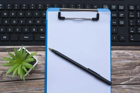 Home office workspace with black keyboard, blue clipboard, pen and potted plant Foto stock