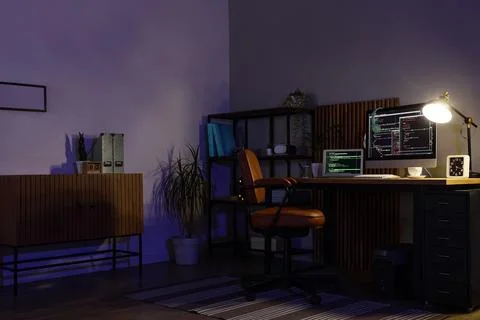 Home office workspace with computer screens showing code at night Stock Photos