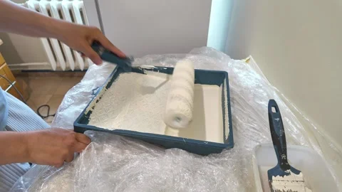 Home painter loading paint roller from tray inside room near radiator Stock Footage 335315511