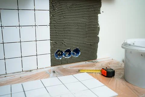 Home renovation process with new white tiles being installed, showing mortar Stock Photos