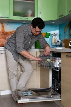 Home routine work, cleaning the kitchen, a young man puts dishes in the dishw Foto stock