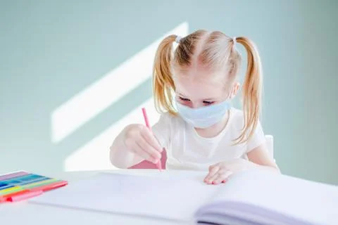 Home schooling learning during virus pandemic. Little girl drawing at home, w Stock Photos