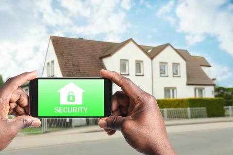 Home security system. African American man with smartphone near his house o.. Stock Photos