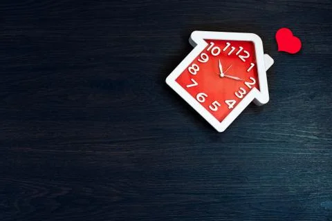Home shape clock on floor background with red heart icon. Happy life and Fami Photos