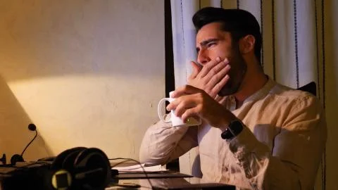 Home worker yawning at computer drinking coffee or tea Foto stock