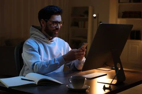 Home workplace. Happy man using smartphone while working with computer at w.. Foto stock