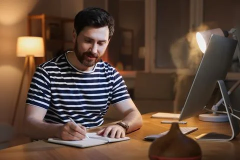 Home workplace. Man taking notes while working with computer at wooden desk.. Stock Photos