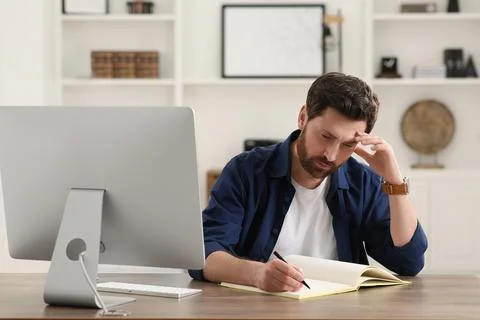 Home workplace. Man taking notes near computer at wooden desk in room Stock Photos