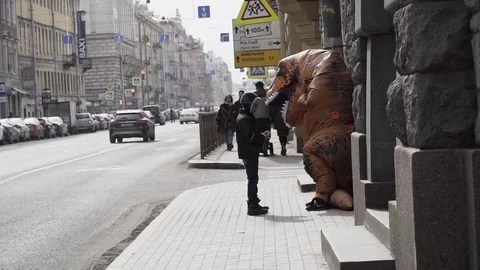 Homeless boy interacts with man in dinosaur mascot costume at sidewalk Stock Footage 84930063
