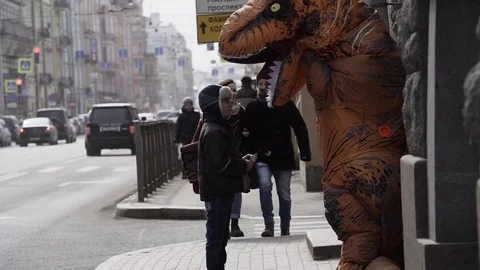 Homeless child interacts with man in dinosaur mascot costume at sidewalk Stock Footage 84930127