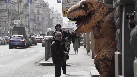 Homeless child talking to man in dinosaur mascot costume at sidewalk Stock Footage 84929945