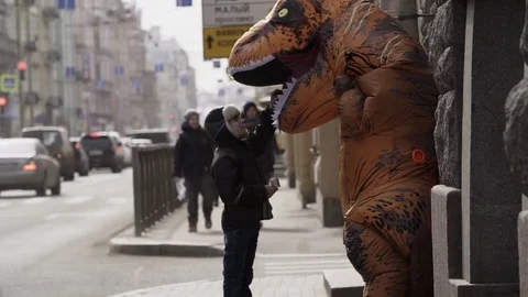 Homeless child talking to man in t rex mascot costume at sidewalk Stock Footage 84930152