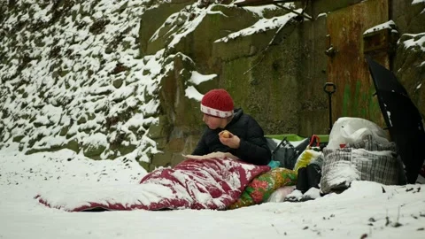 Homeless food eats pastry ham meat sleeping bag poor park winter snow frost Stock Footage 148404698