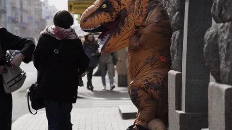 Homeless kid interacts with man in dinosaur mascot costume at sidewalk Stock Footage 84930014
