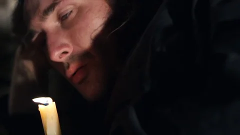 Homeless long-haired man blows out a candle in an abandoned room. Night sleep of Stock Footage 87885852