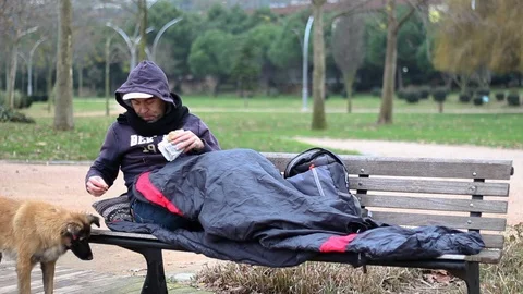 Homeless man eats a snack and shares his food with the dog Stock Footage 100137917