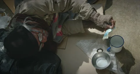 Homeless man is lying down on the sidewalk and asking for money Stock Footage 139847685