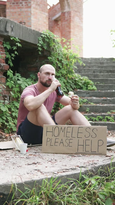 A homeless man with a sign asking for help eats a sandwich and drinks water. Stock Footage 306751871
