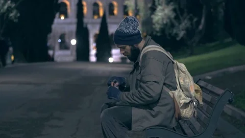 Homeless man sitting on a bench counts money at night Stock Footage 84035493