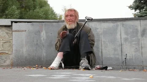 Homeless man sitting on the pavement with a bandaged leg and begging passers Stock Footage