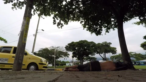 Homeless person sleeping on the sidewalk while cars drive down a street Video stock 150820706
