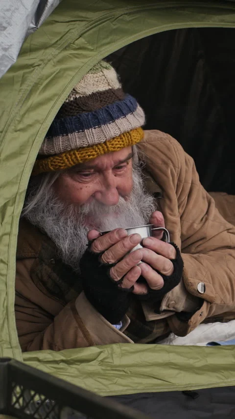 Homeless Senior Man Drinking Steaming Beverage in Street Tent Stock Footage 345703710
