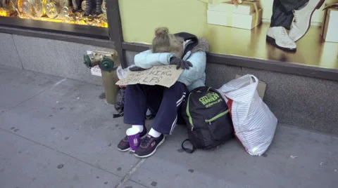 Homeless woman with help sign and backpack sitting on sidewalk on NYC street Stock Footage