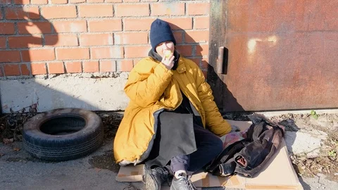 Homeless woman in a yellow old ragged jacket and blue hat is sitting Stock Footage