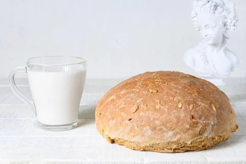 Homemade bread, cup of milk and sculpture on white rustic wooden table Stock-Fotos