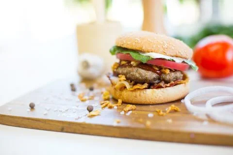 Homemade burger with beef, fried bacon and onion on wooden cutting board Foto stock