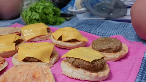 Homemade Cheeseburger Assembly Process on Pink Mat During Outdoor Picnic Stock Footage 341999240