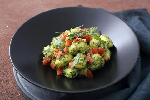 Homemade pesto gnocchi with tomatoes on black plate Stock Photos