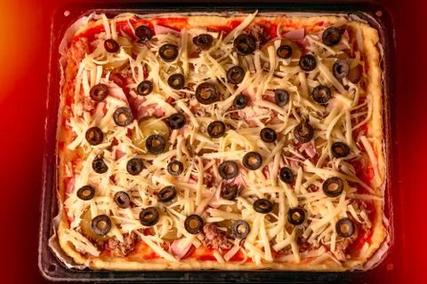 Homemade rectangular pizza with cheese, meat and olives on a baking sheet in  Stock Photos