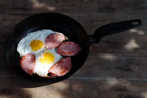 Homemade scrambled eggs with sausage in a pan, wooden background Stock Photos