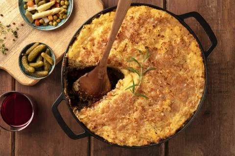 Homemade Shepherd s pie with a missing slice, with pickles and wine on a r... Stock Photos
