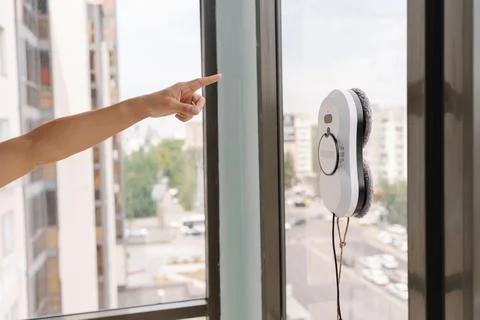 Homemaker gesturing toward robotic window cleaner working on tall glass building Fotos de archivo