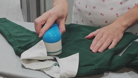 Homemaker using modern electric lint remover on green knit sweater, carefully Stock Footage 348506816