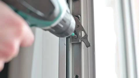 A homeowner uses an electric drill to secure hardware onto a window frame. Stockbeeldmateriaal 337111530