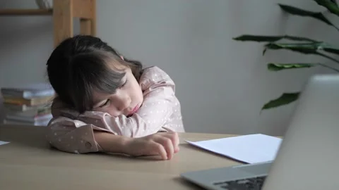 Homeschooling girl kid is lying on wooden table. Child making boring face while Stock Footage