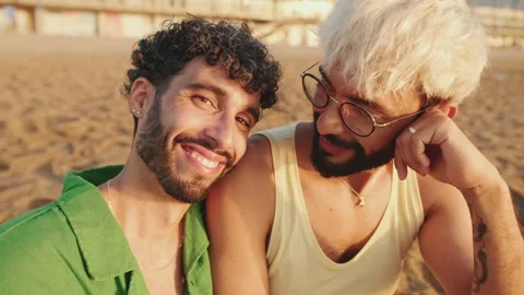 Homosexual couple in love talking while sitting on the beach Stock Footage 252207198
