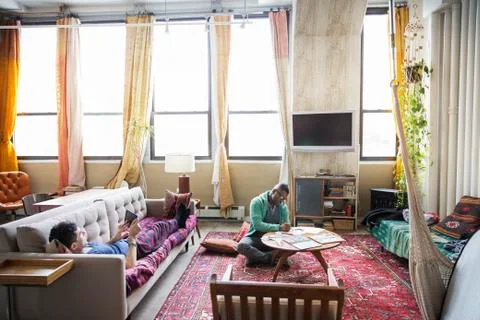 Homosexual man drawing while partner using tablet computer in living room Stock Photos