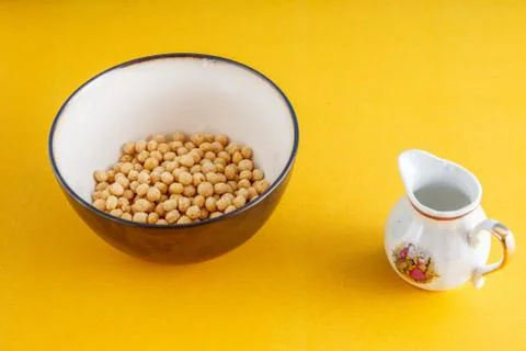 Honey balls of different cereals in a deep bowl and milk on a yellow backgrou Stock Photos