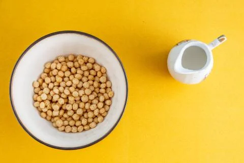 Honey balls of different cereals in a deep bowl and milk on a yellow backgrou Stock Photos