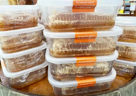 Honey in clear plastic containers stacked for sale, showcasing honeycomb and Stock Photos