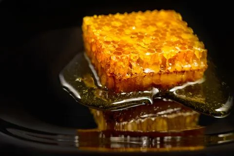 Honey close-up. Square cut piece of honeycomb with honey on a black background Stock Photos