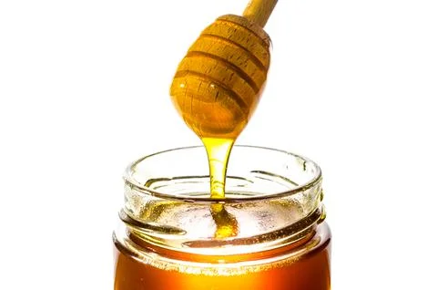 Honey on dipper from a jar Stock Photos