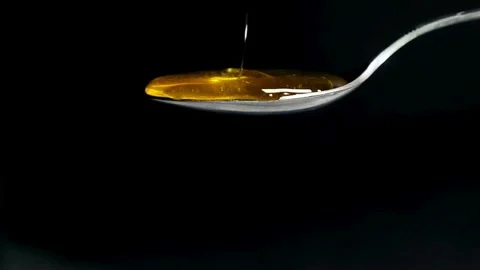 Honey dripping onto a silver spoon in slow motion against black background Stock Footage 332870754
