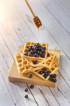 Honey dripping on a stack of Belgian waffles with blueberries in the morning sun Foto stock