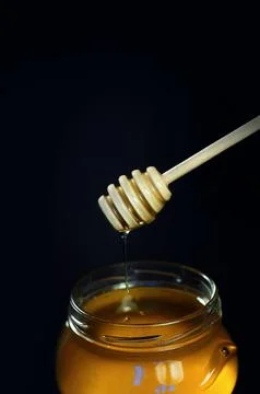 Honey flows down a spoon into a jar on a black background Stock Photos